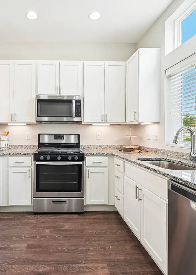 Bright, modern kitchen featuring sleek white cabinets, granite countertops, stainless steel appliances, and elegant wood flooring.