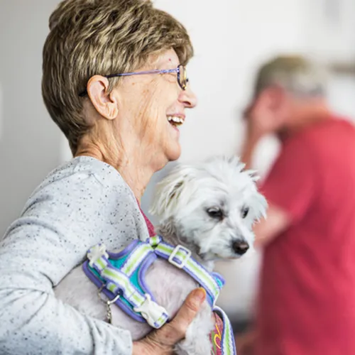 Joyful scene with a woman holding her small, white dog, exuding warmth and happiness in a welcoming environment.