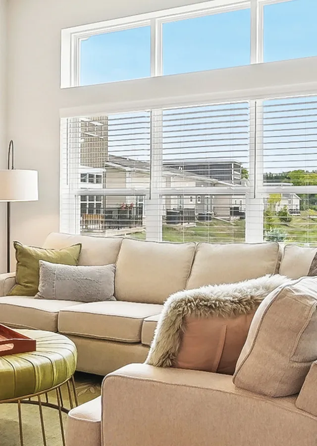 Bright and inviting living room with plush beige sofa, chic green ottoman, and large windows offering a scenic view.