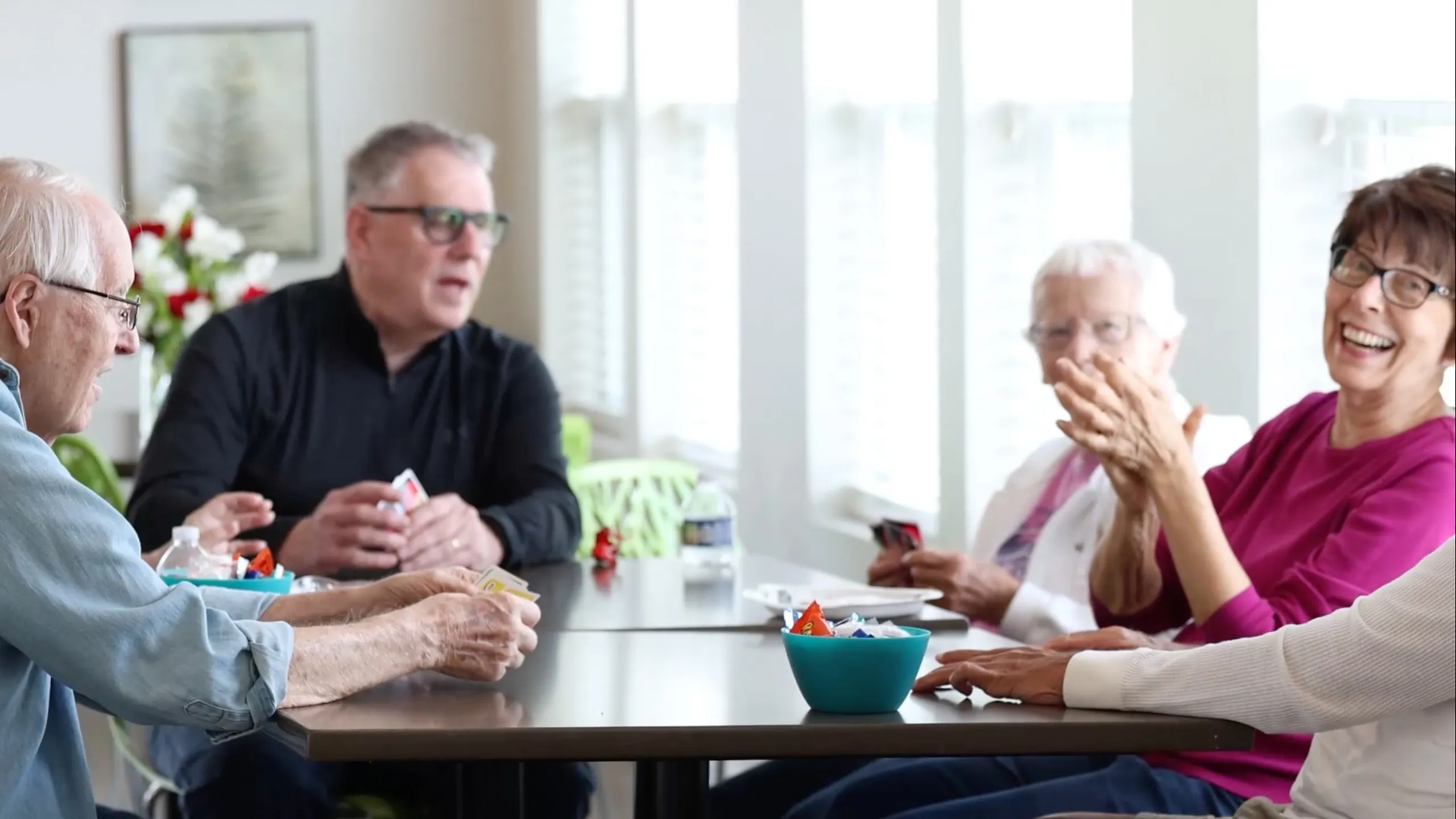 Vibrant senior community gathering around a table, enjoying a lively card game in a sunlit room.