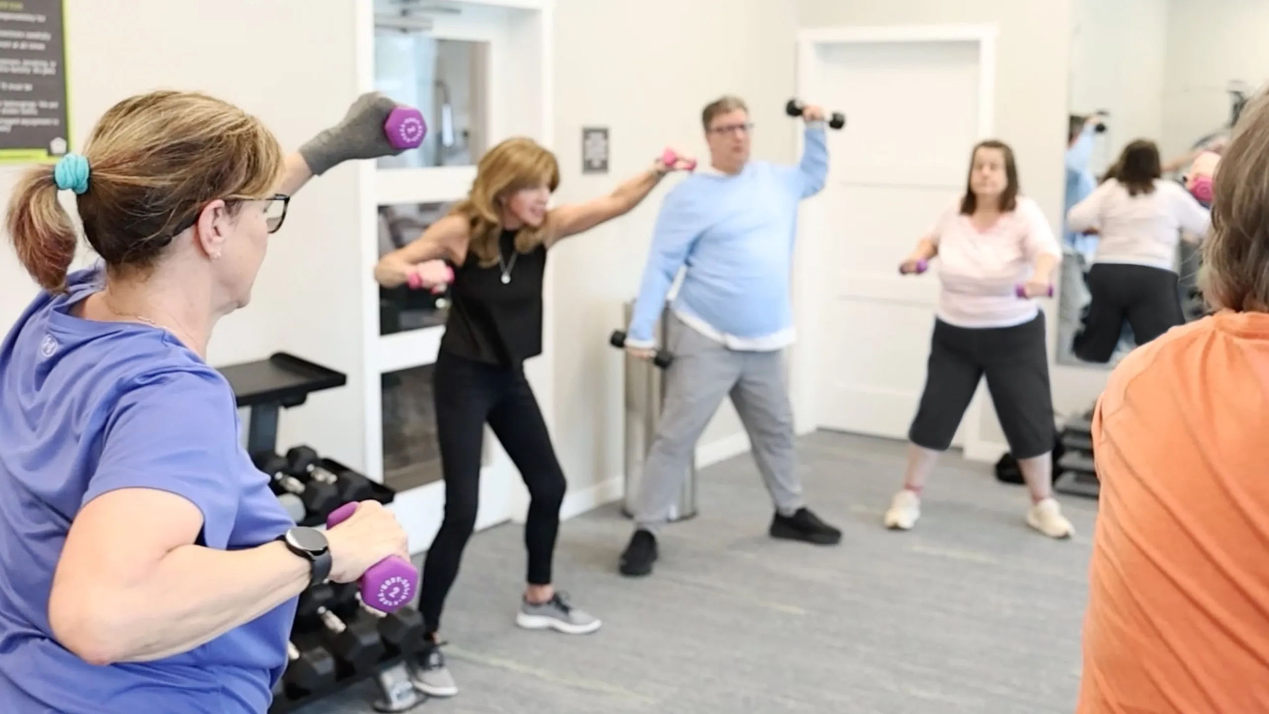 Engaging fitness class with motivated adults lifting weights in a bright, modern gym.