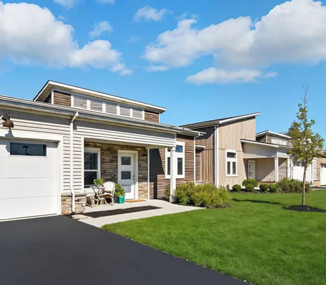 Charming modern homes with eco-friendly designs, featuring manicured lawns and sunlit exteriors under a clear blue sky.