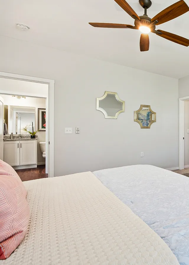 Elegant bedroom with cozy bedding, tasteful wall decor, and a ceiling fan, leading into a modern en-suite bathroom.
