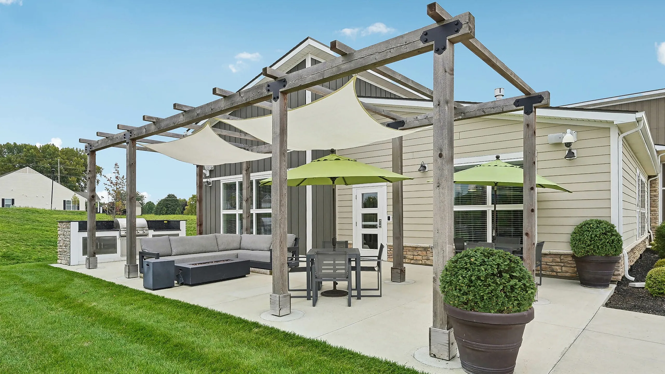 Charming outdoor patio with pergola, stylish sectional, and dining set, surrounded by lush greenery and modern architecture.