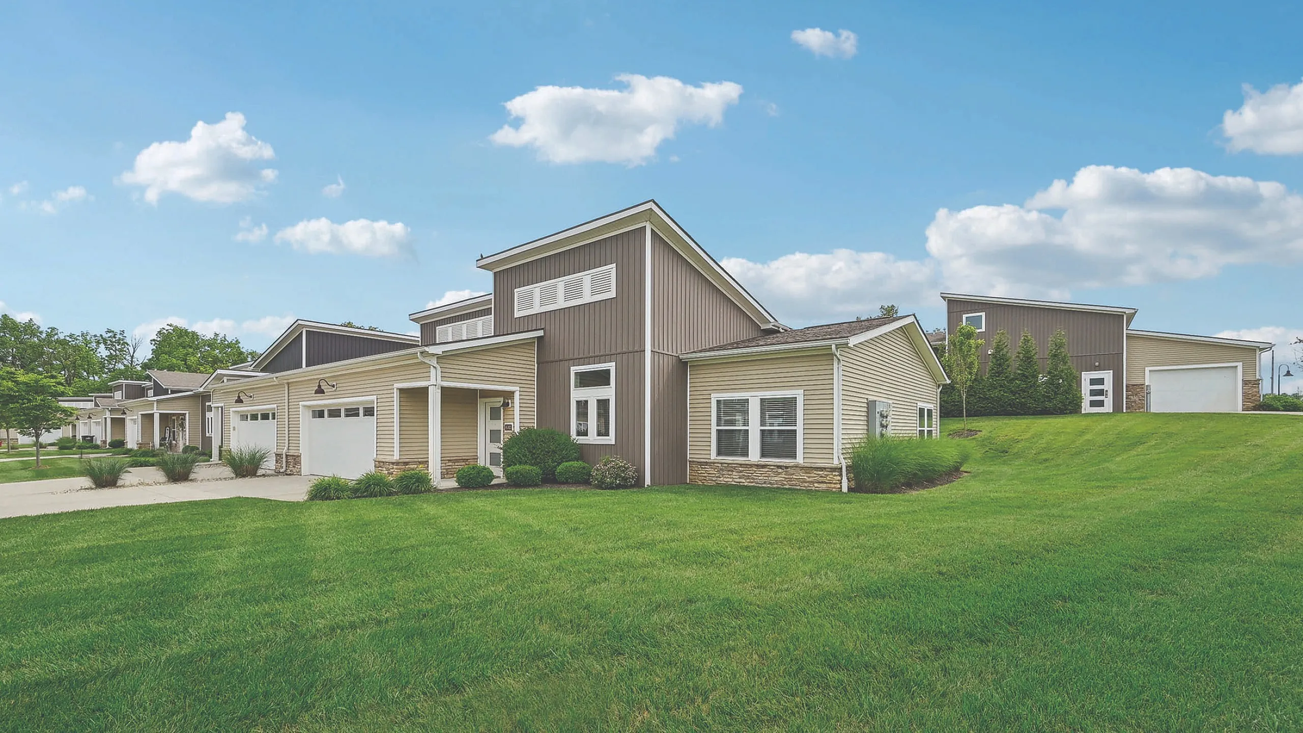 Charming modern homes with large green lawns and sleek architecture under a clear blue sky.