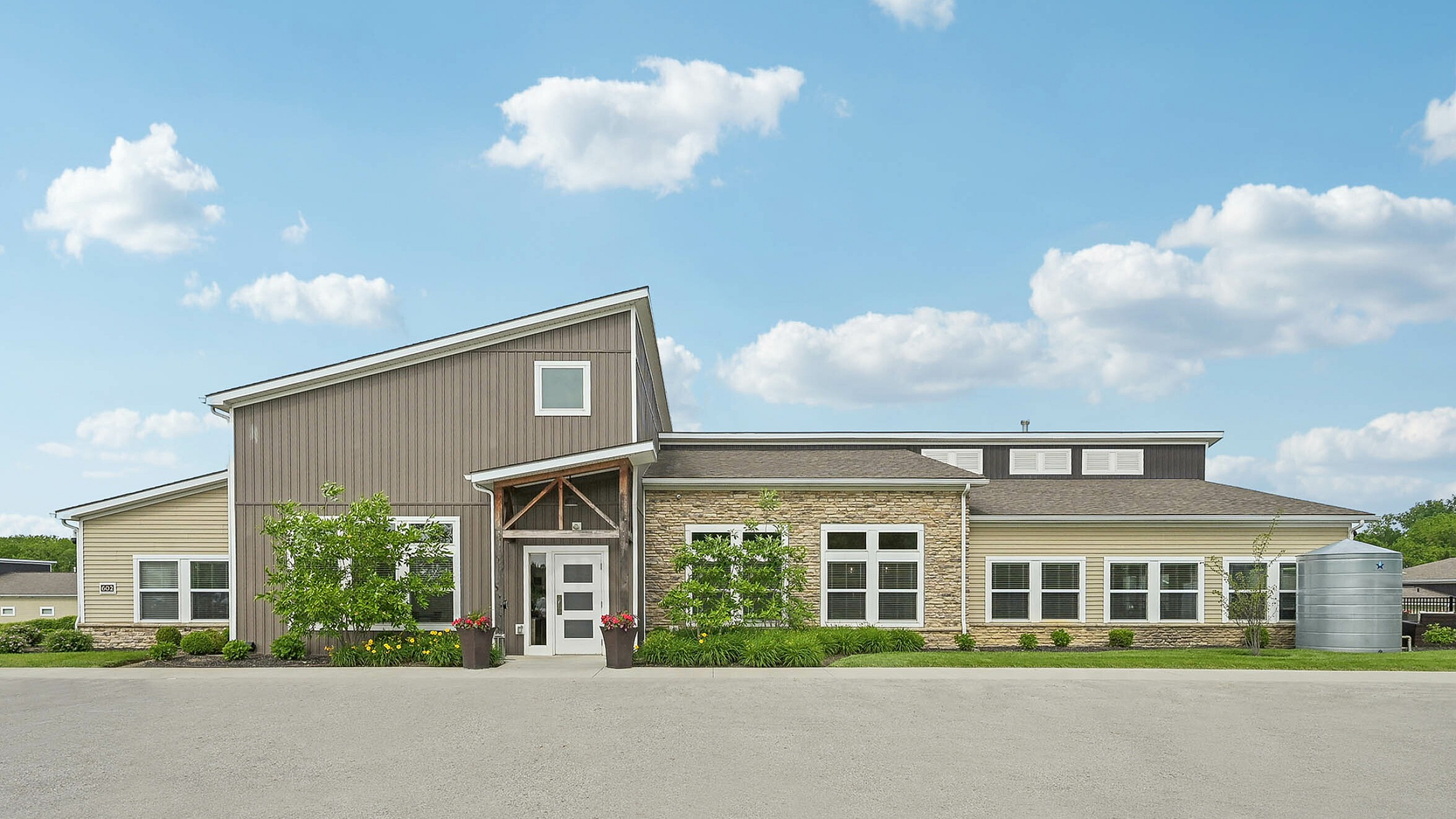 Charming modern building with a rustic exterior, surrounded by lush greenery and a clear blue sky.