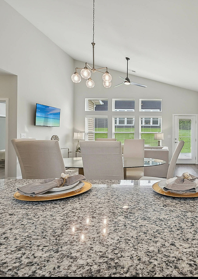 Elegant open-concept living room with modern chandelier, sleek granite kitchen countertop, and designer dining setup.