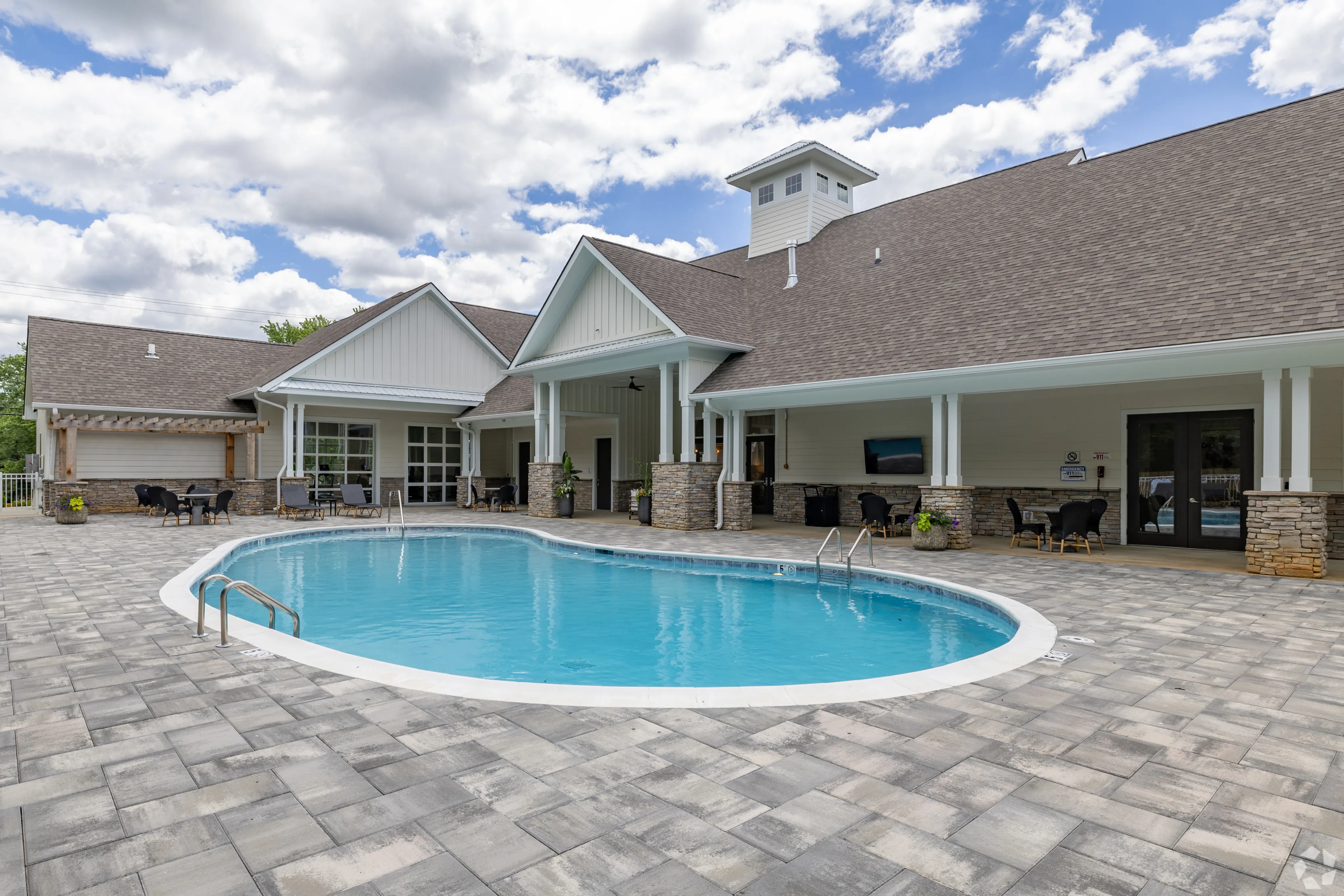 Charming community pool area with elegant stone patio, modern clubhouse, and cozy outdoor seating.