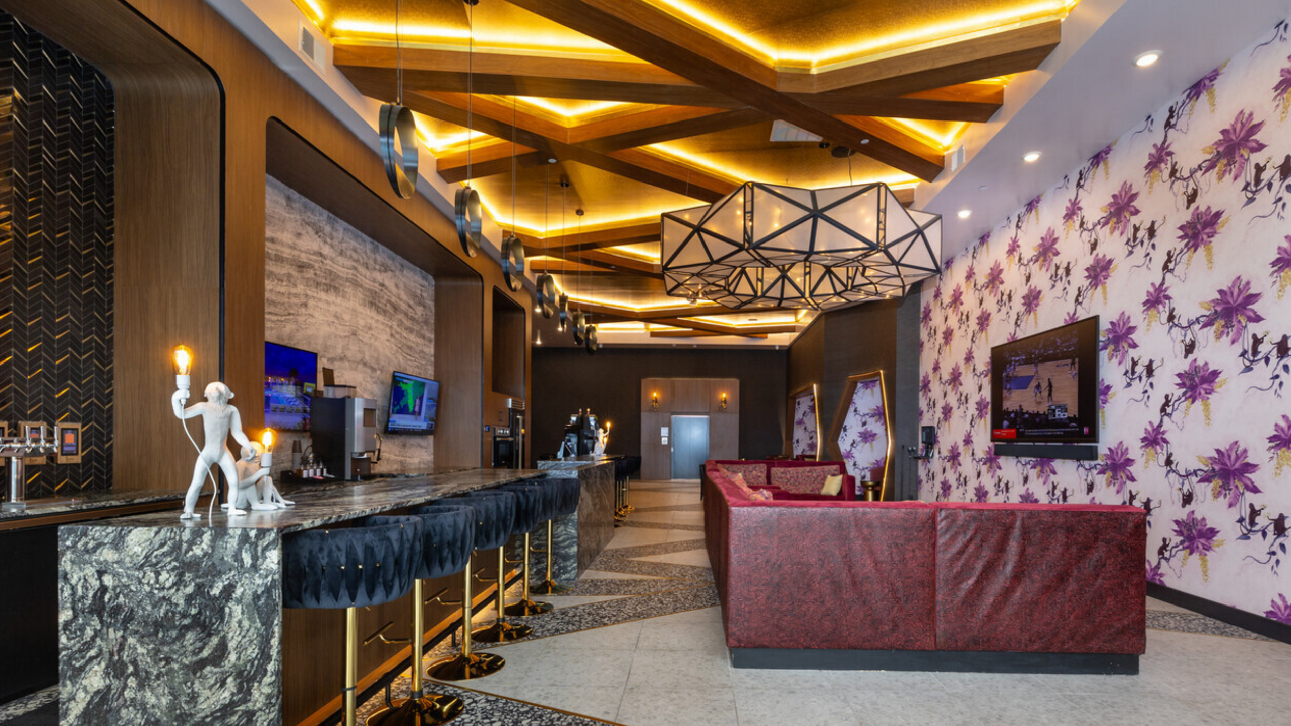 Luxurious lounge featuring elegant marble bar, plush red seating, and vibrant floral wallpaper. Modern lighting and multiple TVs enhance the sophisticated atmosphere.