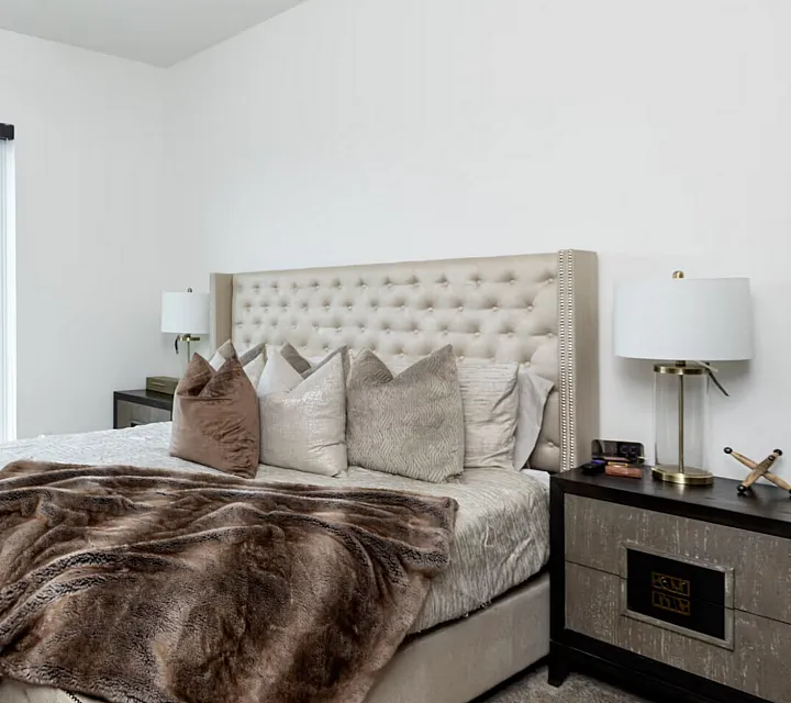 Elegant bedroom with plush neutral bedding, large sunlit window, and sleek modern decor.