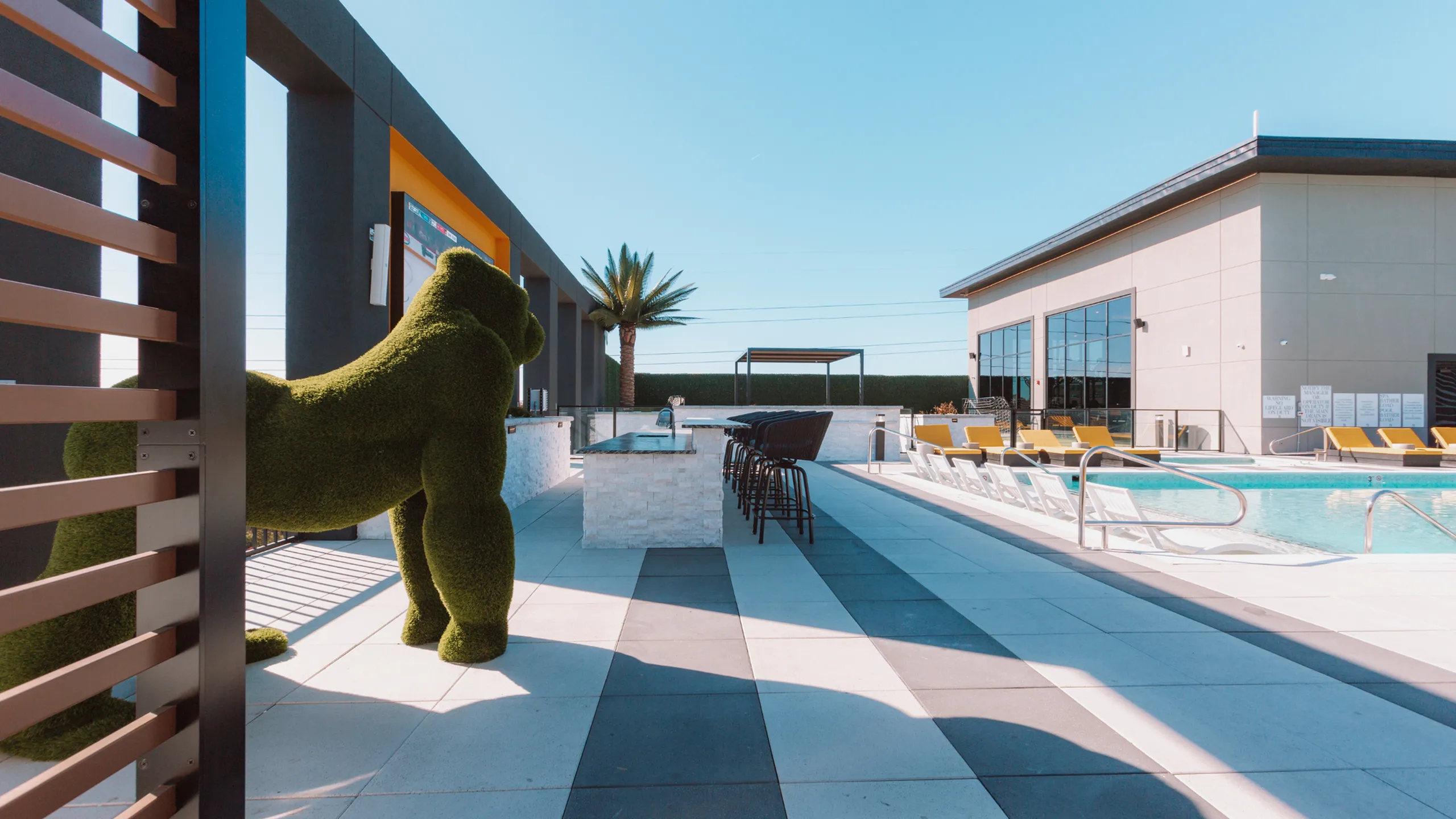 Luxurious outdoor patio featuring modern seating, a sparkling swimming pool, and unique green gorilla sculpture under a clear blue sky.