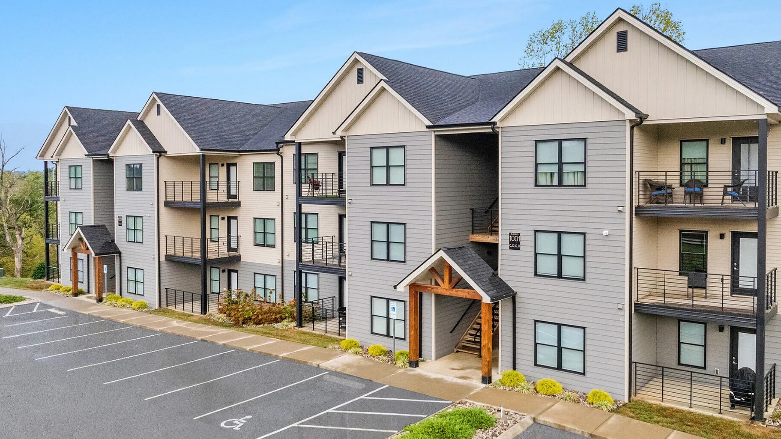 Modern apartment building showcasing stylish architecture with spacious balconies, surrounded by greenery and ample parking space.