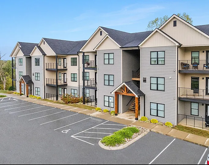 Modern three-story apartment building with stylish balconies, ample parking space, and lush green surroundings.