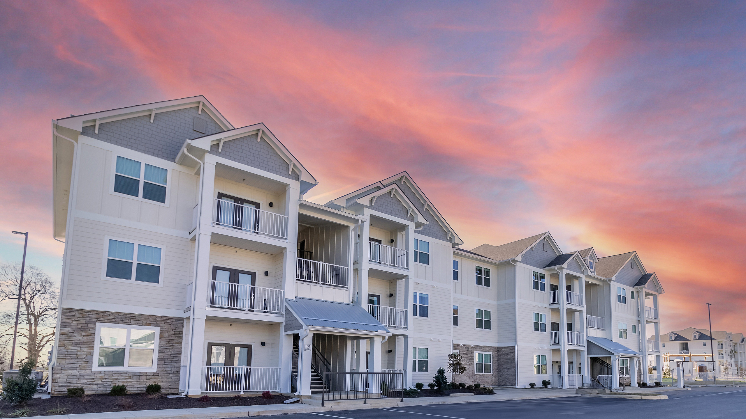Charming modern apartment complex under a vibrant sunset sky, featuring spacious balconies and contemporary design.
