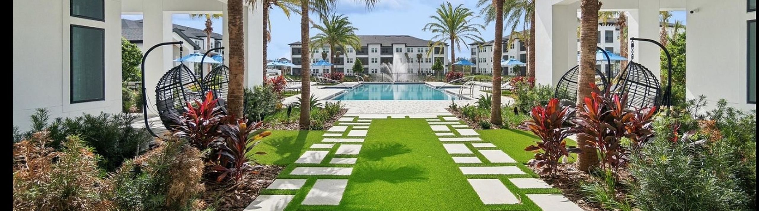 Luxurious tropical oasis with palm trees, manicured lawn, and modern pool featuring stylish lounging areas in a resort-style apartment complex.