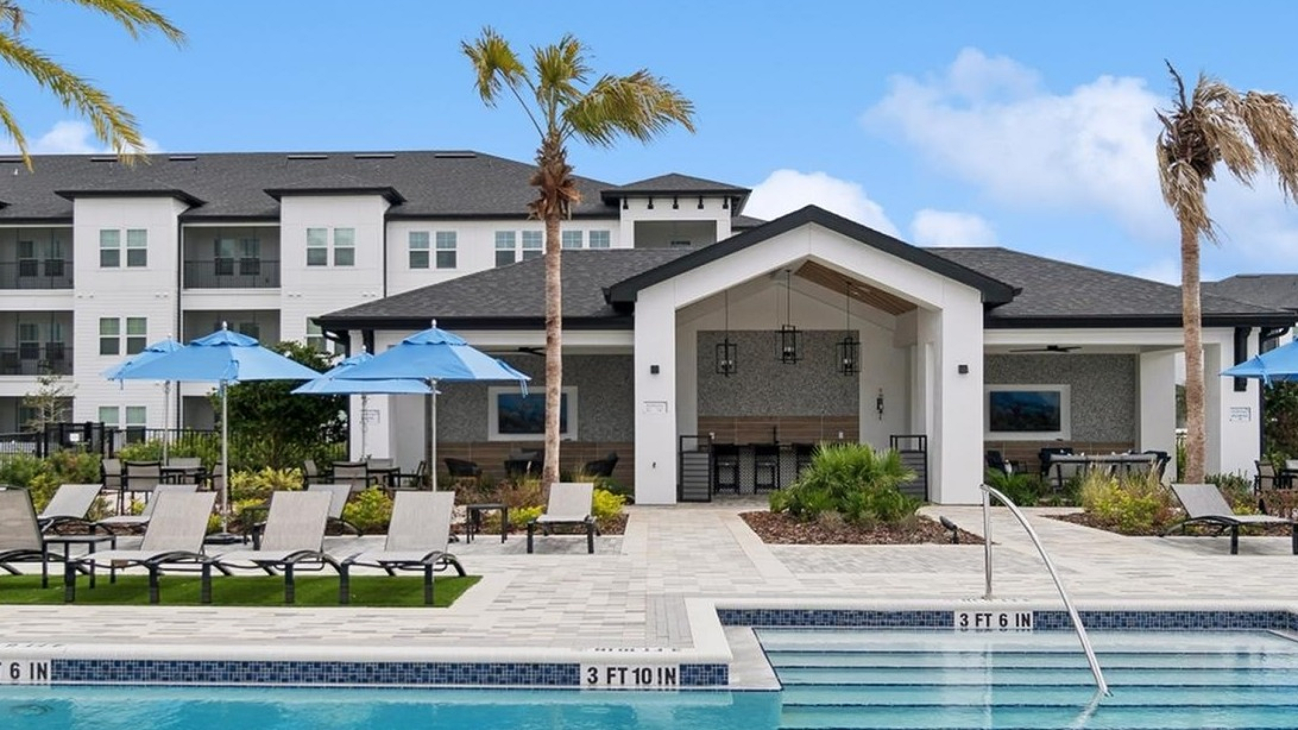 Luxurious apartment complex featuring a sparkling pool, stylish sun loungers, and elegant outdoor patio with bright blue umbrellas.