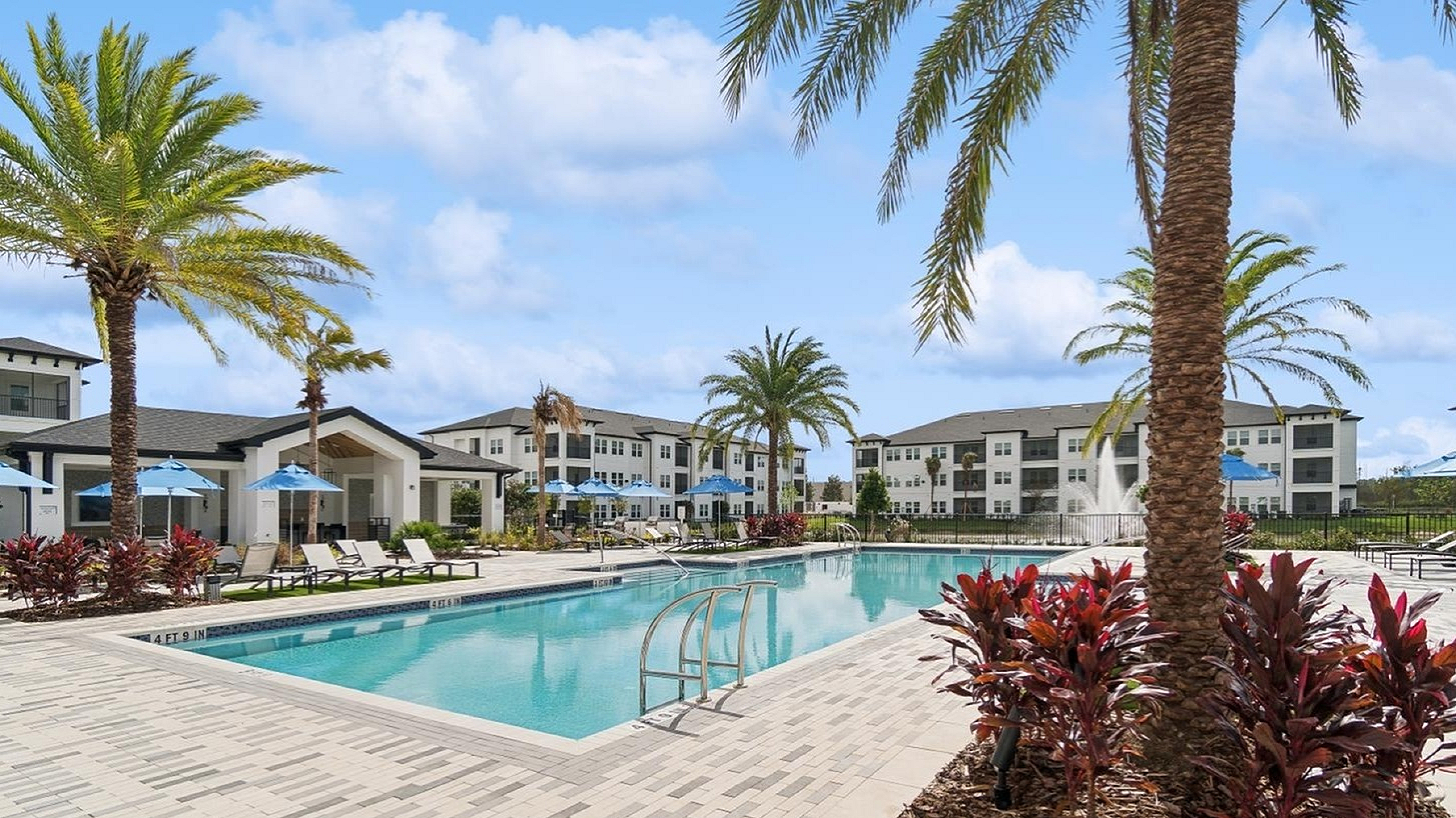 Luxurious apartment complex with a stunning poolside view, surrounded by palm trees and stylish loungers, perfect for relaxation.