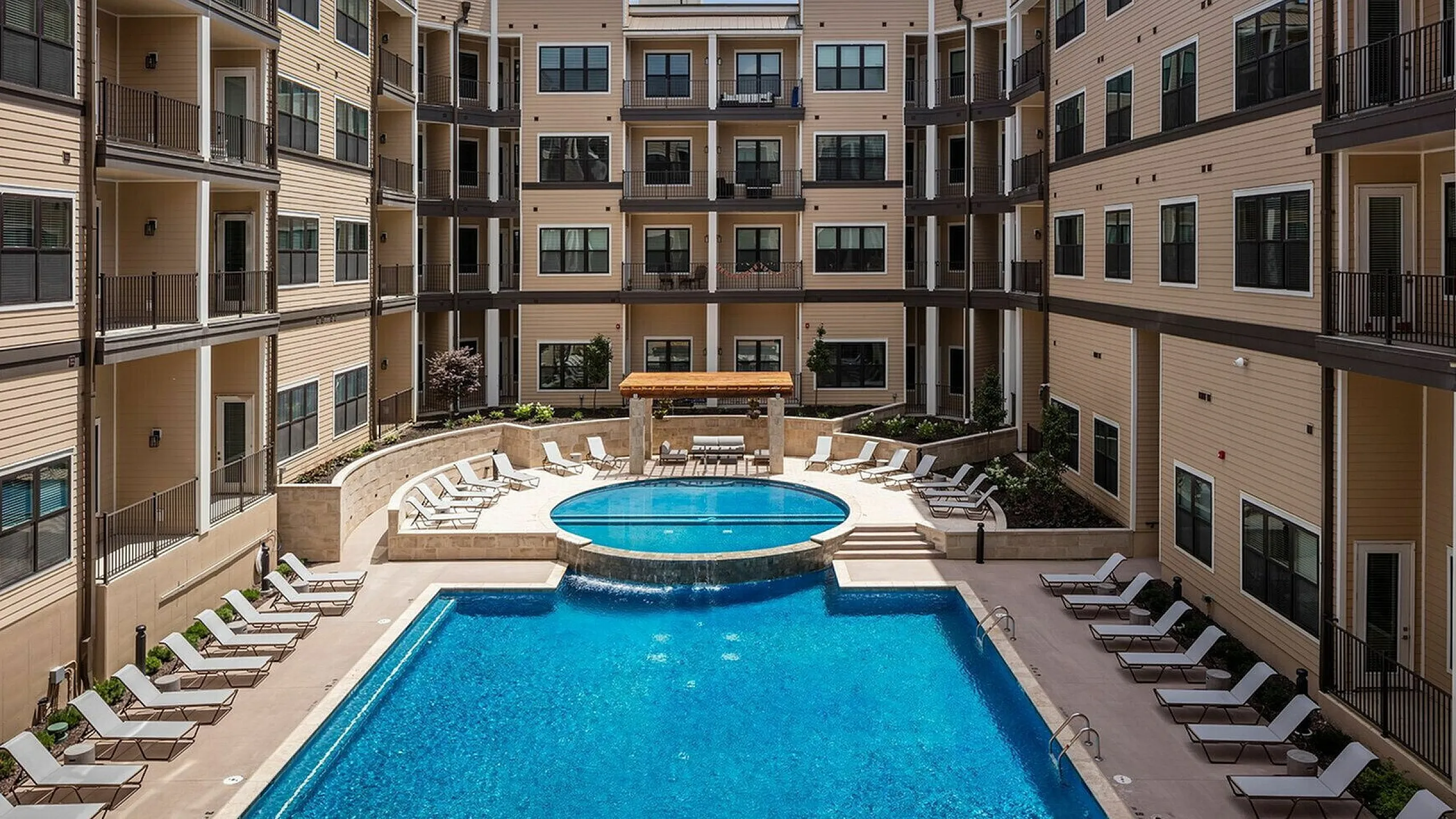 Luxurious apartment complex featuring a pristine swimming pool, sun loungers, and modern balconies, ideal for relaxation and leisure.