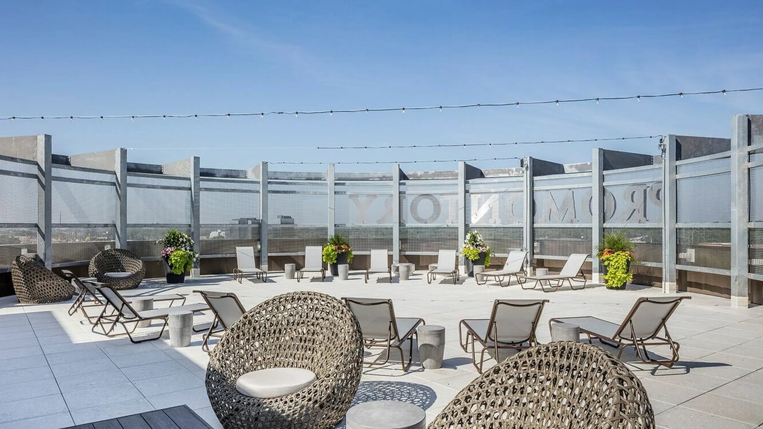 Contemporary rooftop terrace with modern lounge chairs, stylish woven seating, and vibrant potted plants under a clear blue sky.