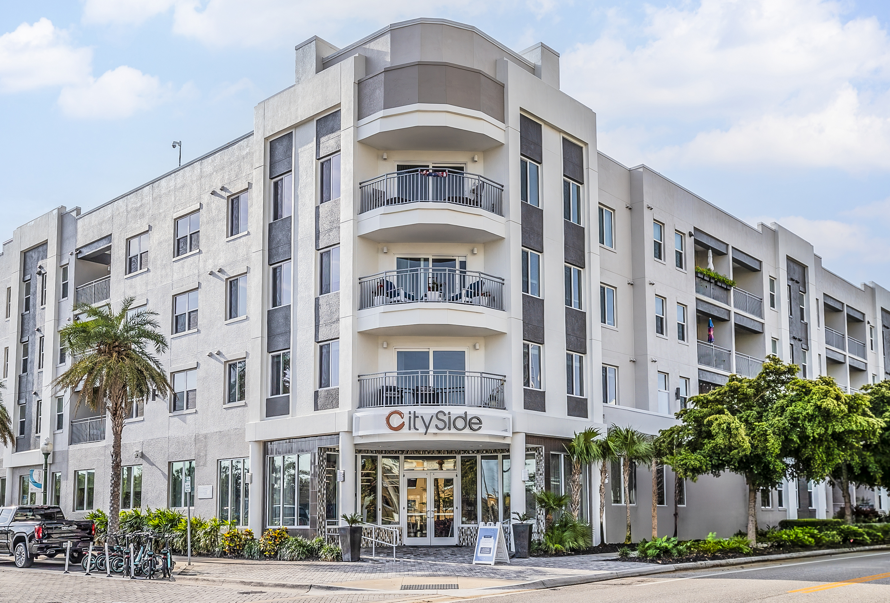 Modern apartment building exterior with sleek design, large balconies, and inviting entrance, surrounded by lush greenery.