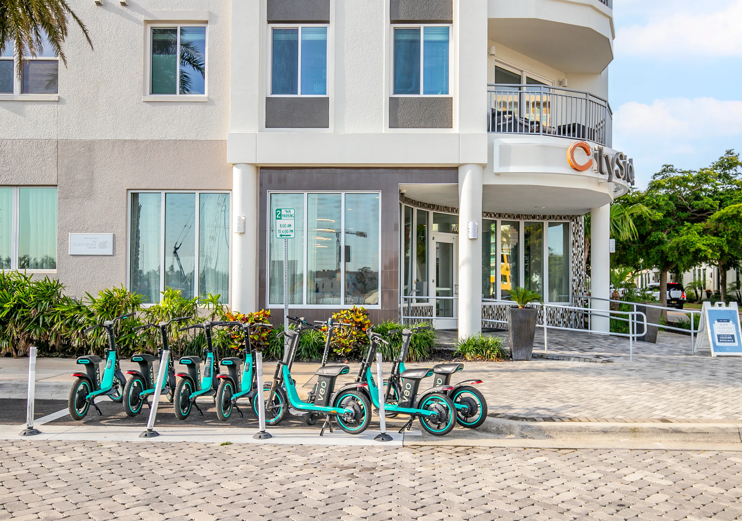 Modern apartment building entrance with stylish architecture, enhanced by a row of vibrant electric scooters for an eco-friendly lifestyle.
