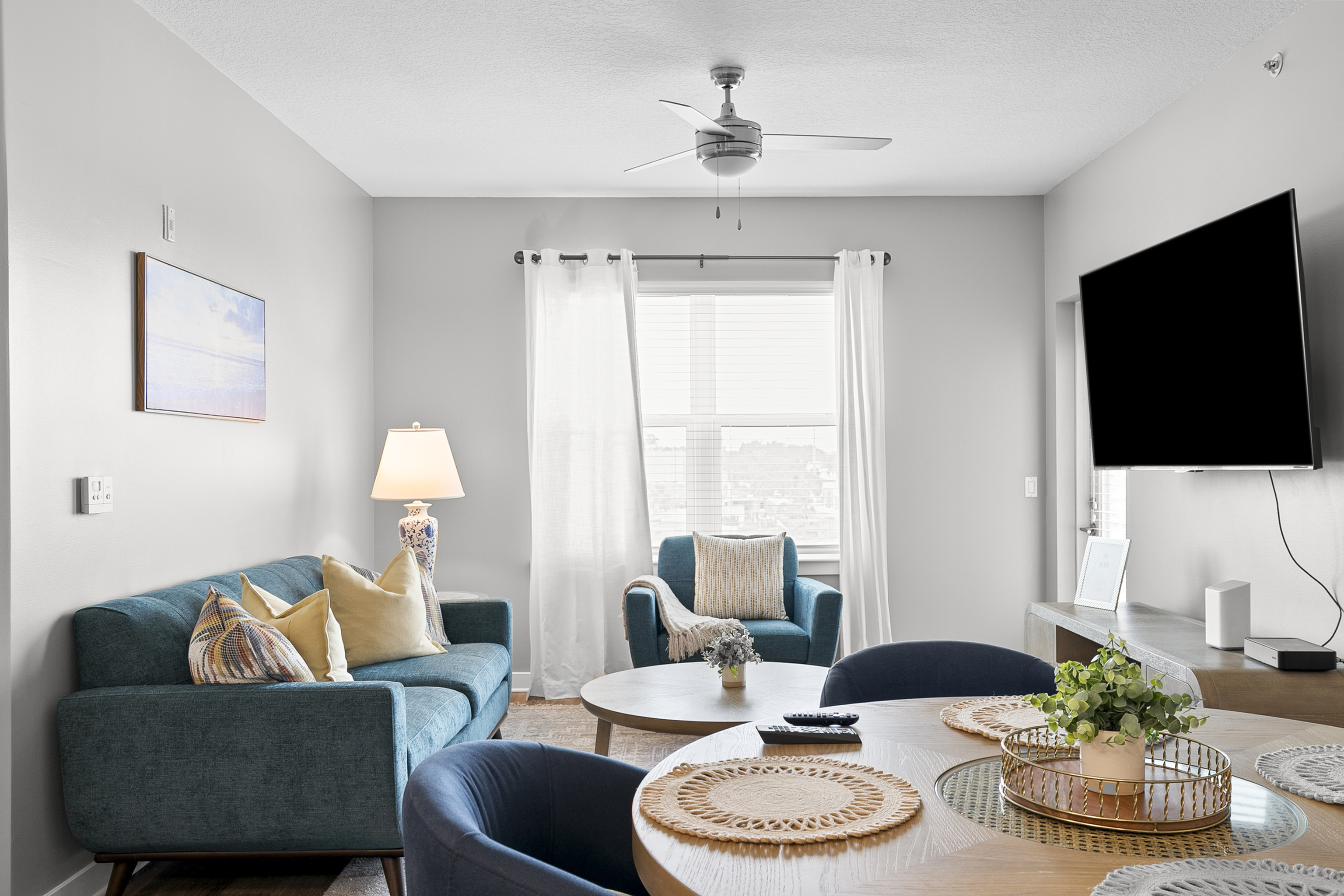 Inviting living room with a modern blue sofa, elegant armchair, and large TV, accentuated by natural light and chic decor.