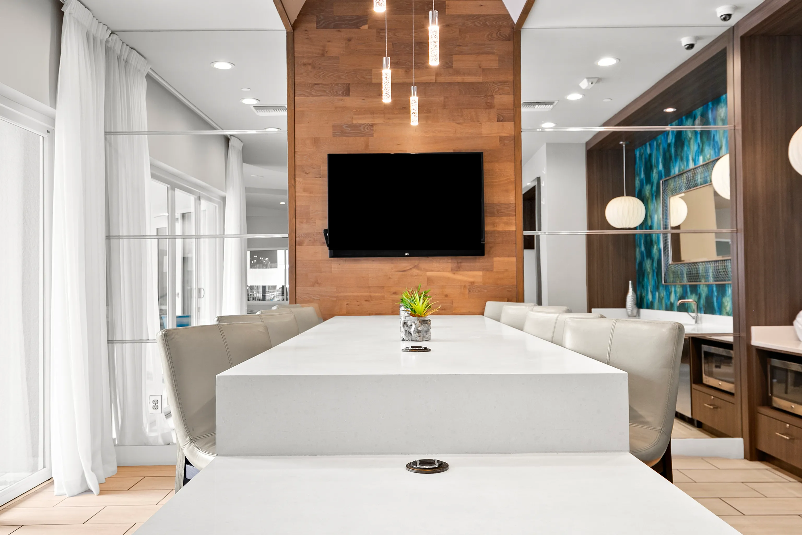 Elegant dining area with a sleek white table, modern lighting, and a warm wood accent wall with a flat-screen TV.