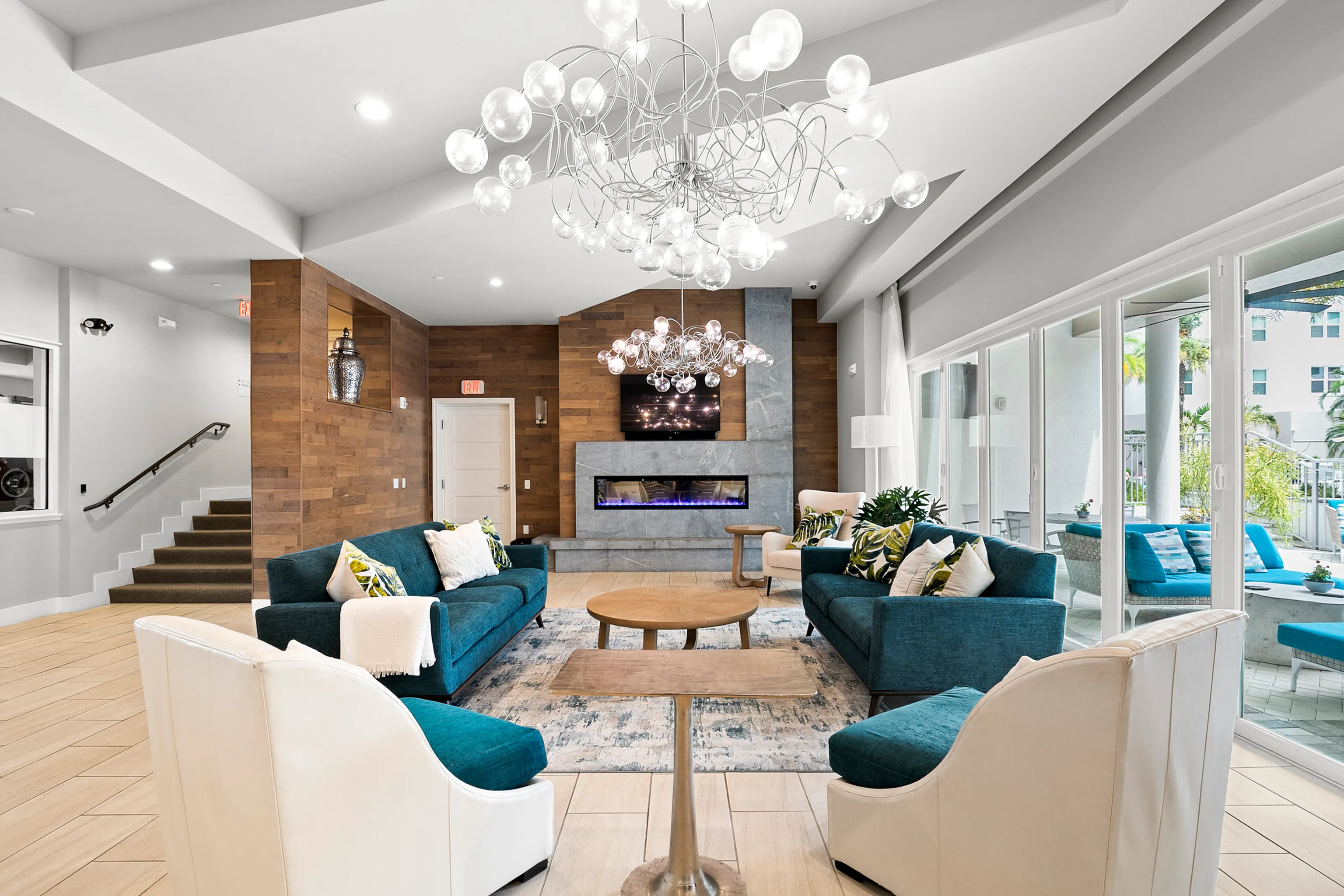 Luxurious living room featuring modern decor with teal sofas, stylish chandelier, and large windows showcasing natural light.