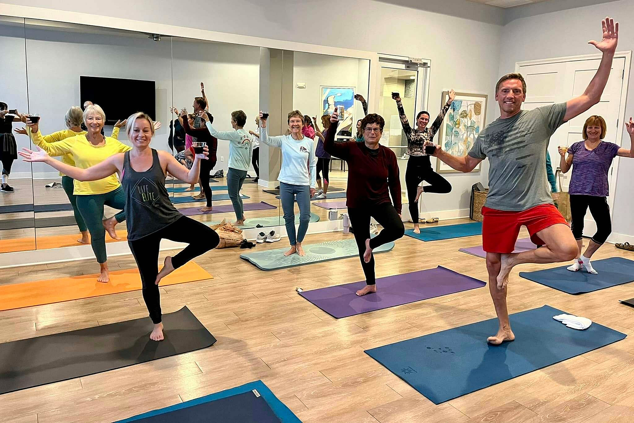 Enthusiastic yoga class enjoying a cheerful session in a bright, mirrored studio, showcasing balance and community spirit.