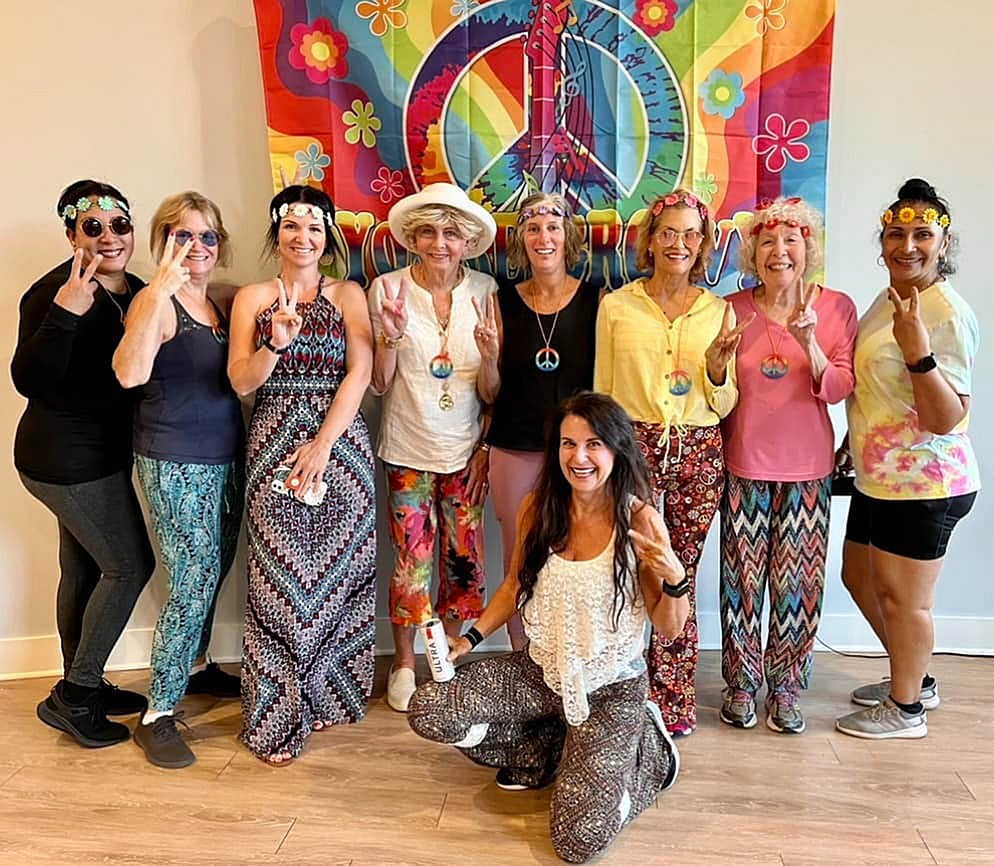 Joyful group of people embracing a retro style, wearing colorful and patterned outfits with peace signs and flower headbands, posing in front of a vibrant peace symbol backdrop.