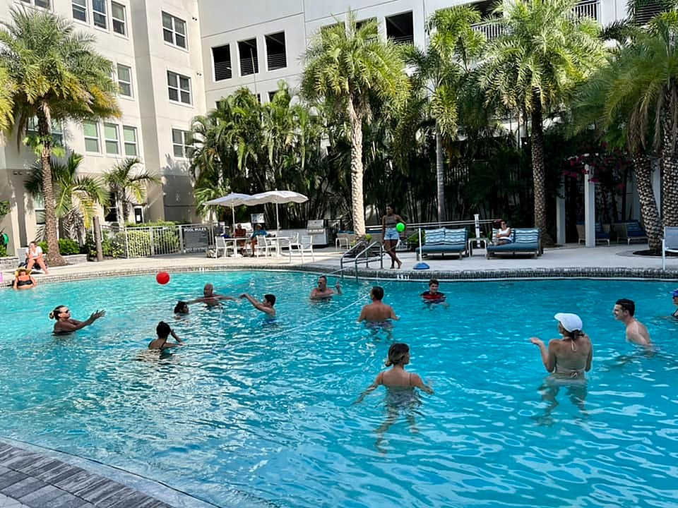 Inviting pool area surrounded by lush palm trees at a luxury apartment complex, showcasing residents enjoying a sunny day swimming and relaxing.