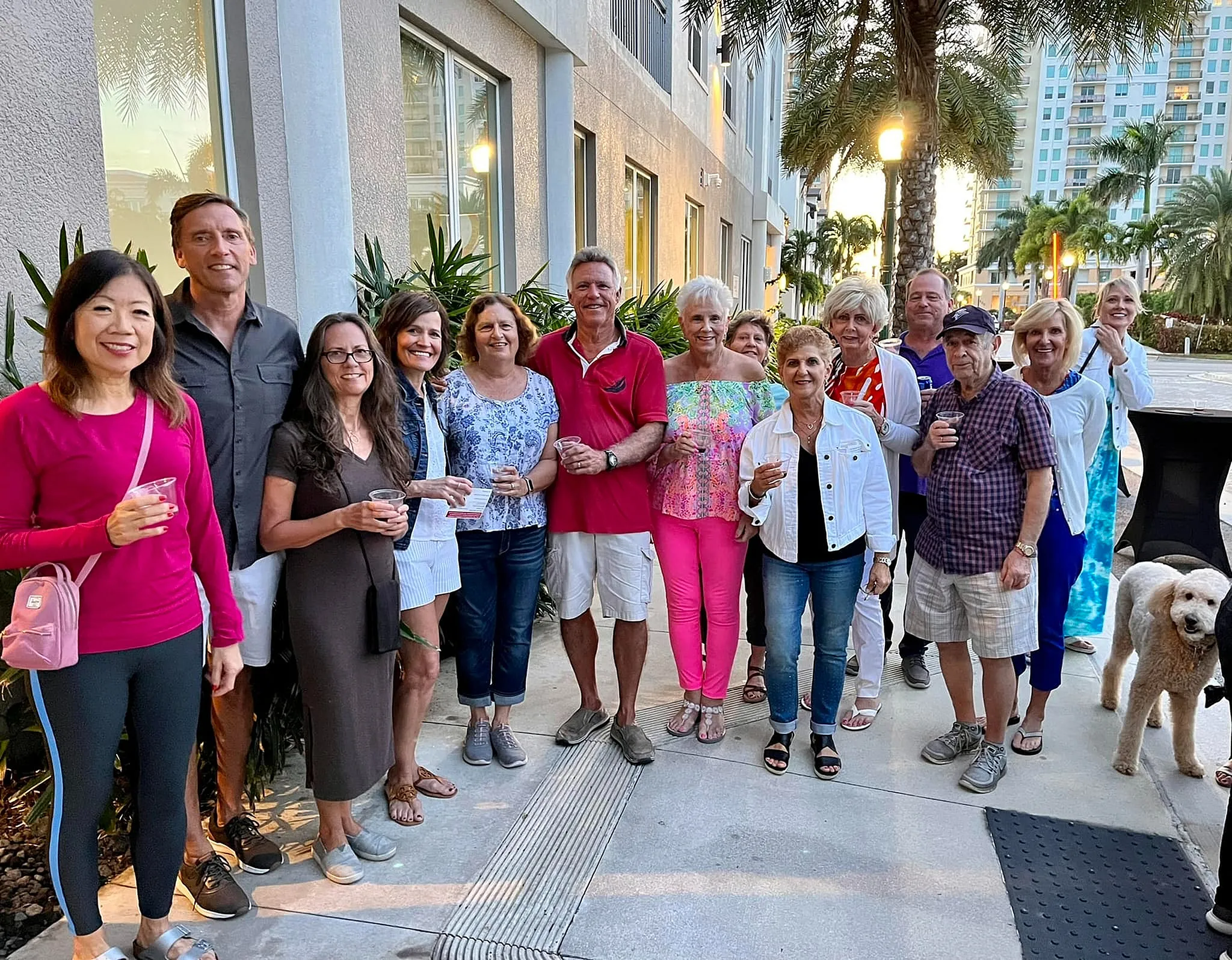 Friendly gathering outside a modern apartment complex with smiling residents enjoying a sunny day, lush greenery, and a welcoming neighborhood vibe.