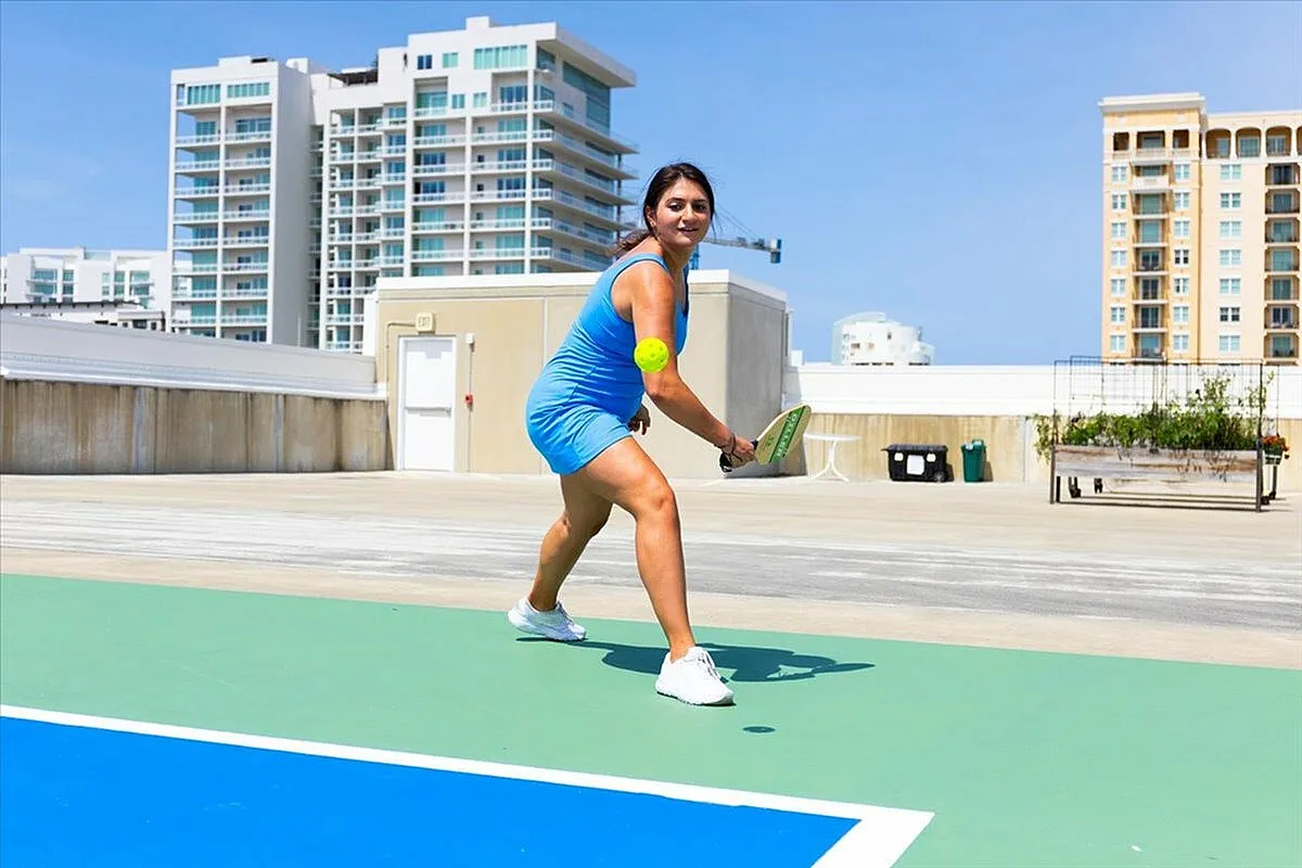 Dynamic scene of a woman enjoying pickleball on a modern rooftop court, with stylish urban apartments in the background.