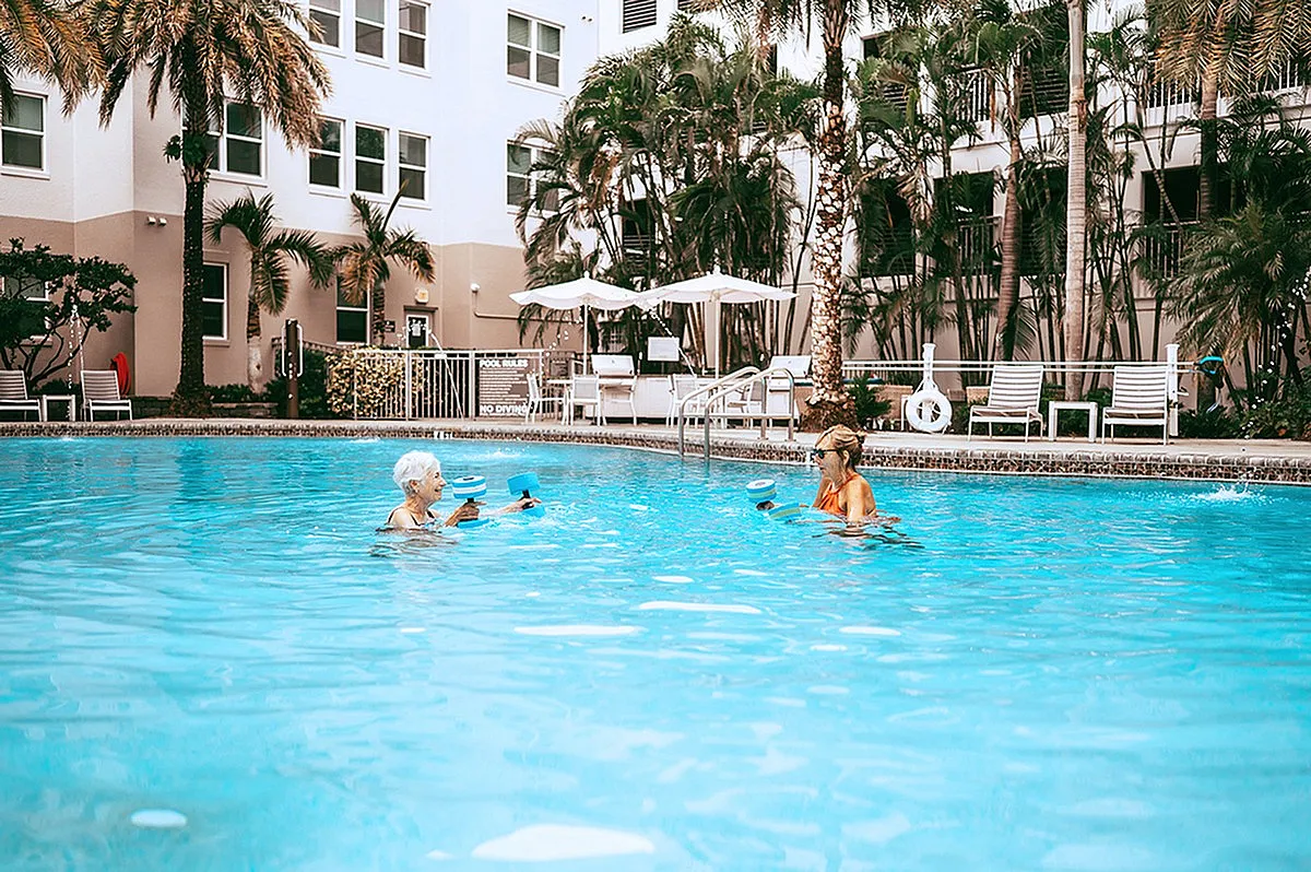 Inviting apartment pool with residents enjoying water exercise amidst lush palm trees and cozy lounge areas.