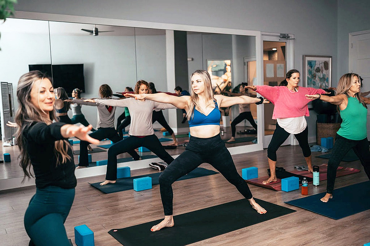 Inviting yoga studio with a mirrored wall, showcasing a group of women in a dynamic warrior pose on mats, fostering harmony and wellness.