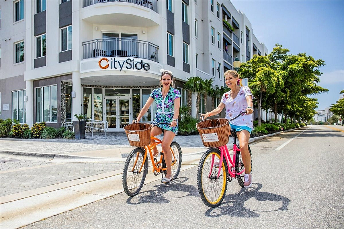 Vibrant lifestyle at CitySide apartments featuring two people joyfully biking in front of modern architecture and scenic greenery.