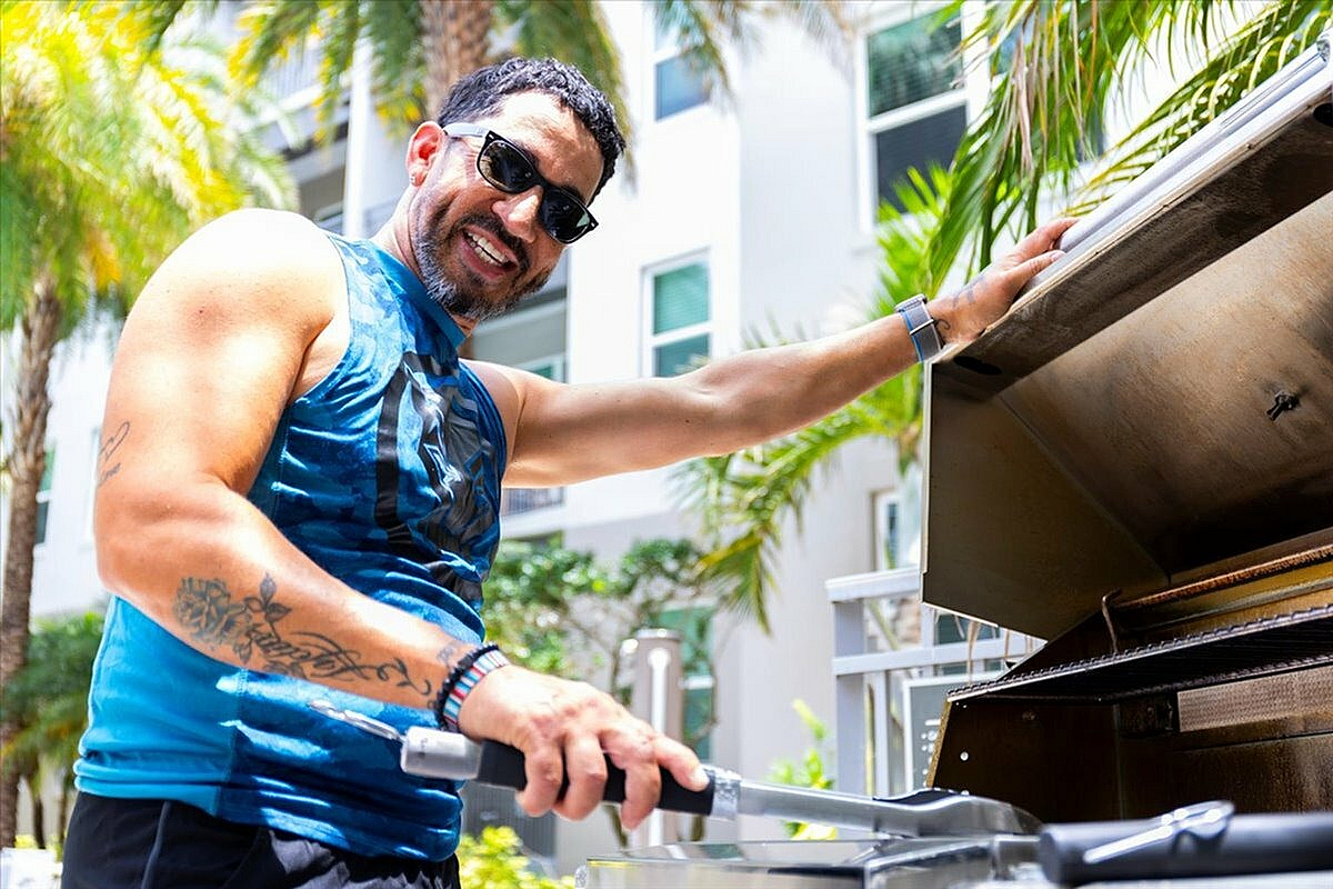 Smiling person grilling outdoors, surrounded by lush greenery and modern architecture, enjoying sunny weather. | City Side Apartments | Sarasota, FL