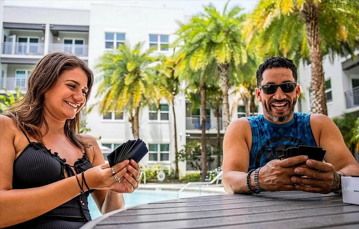 Two people enjoying a card game by a poolside in a vibrant apartment complex with palm trees in the background. | City Side Apartments | Sarasota, FL