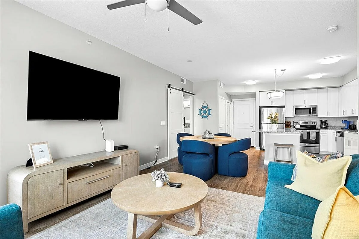Chic modern living space featuring a vibrant blue sofa, sleek wall-mounted TV, elegant dining area, and stylish kitchen with stainless steel appliances. | City Side Apartments | Sarasota, FL