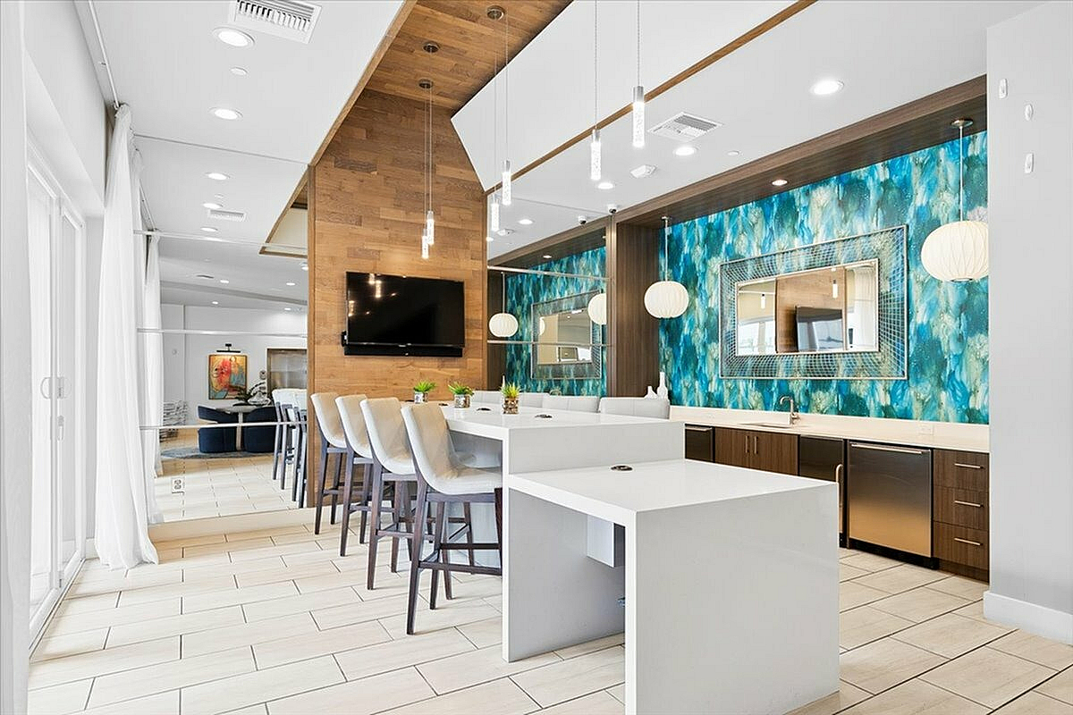 Modern apartment interior featuring a chic open kitchen with sleek white countertops, a vibrant blue accent wall, and spacious seating area under elegant pendant lighting. | City Side Apartments | Sarasota, FL