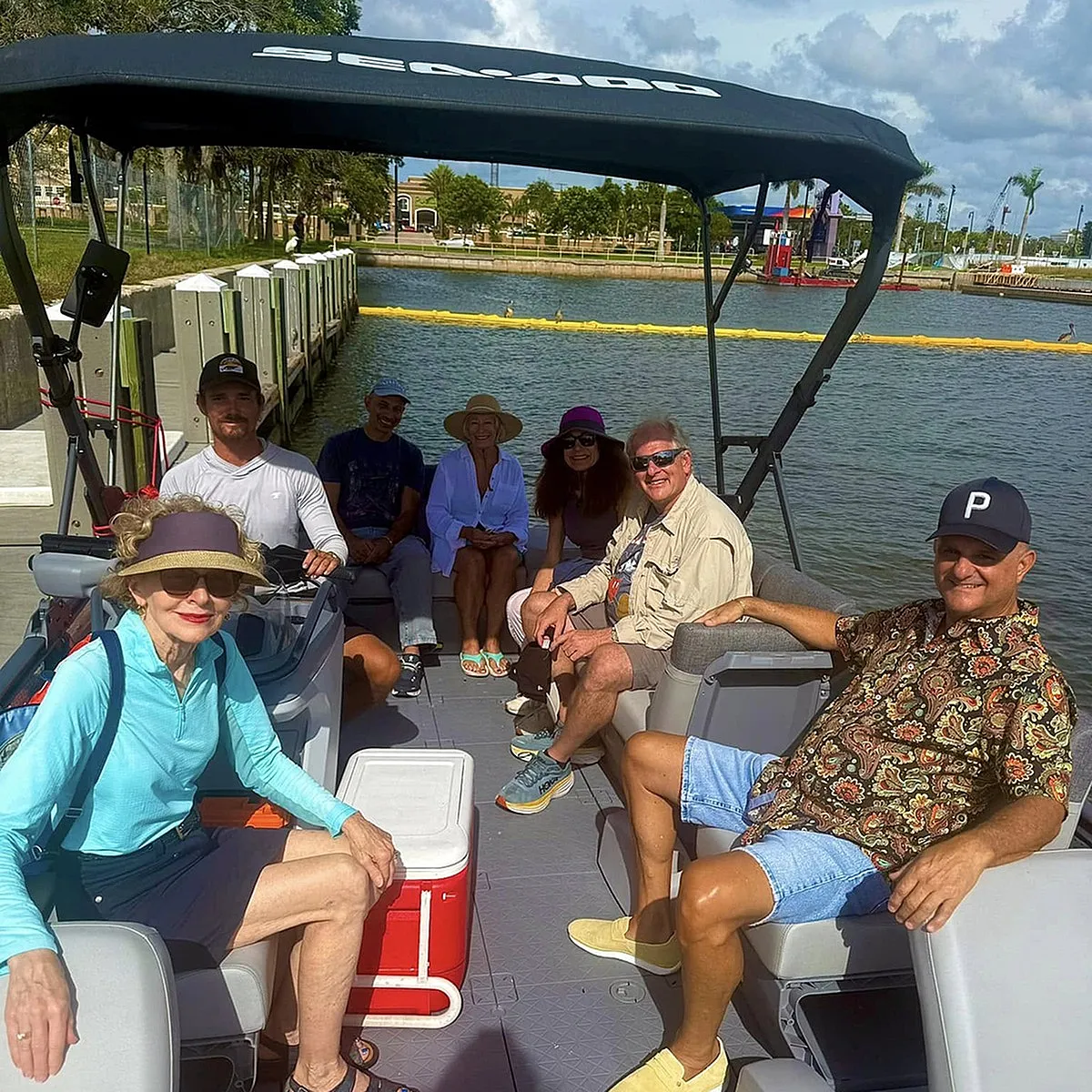 Group of people enjoying a sunny boat ride with smiles and casual attire, set against a serene dockside backdrop.