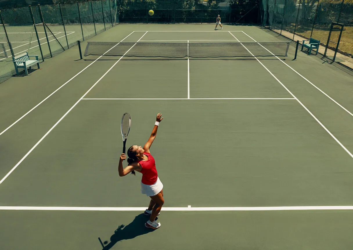 Dynamic tennis match with a player serving powerfully on a sunlit outdoor court.