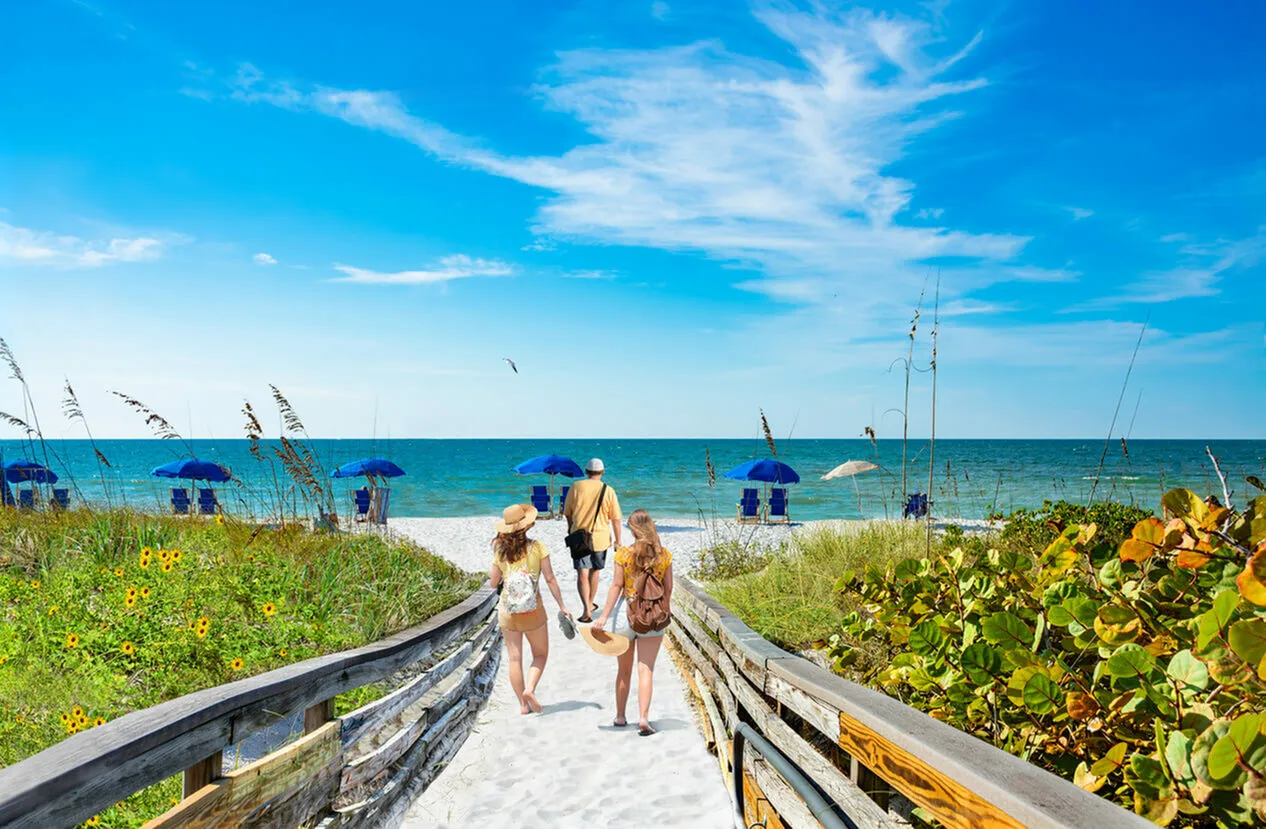 Idyllic beach walkway leading to a sunlit shore with blue umbrellas and gentle waves, perfect for a serene seaside escape.