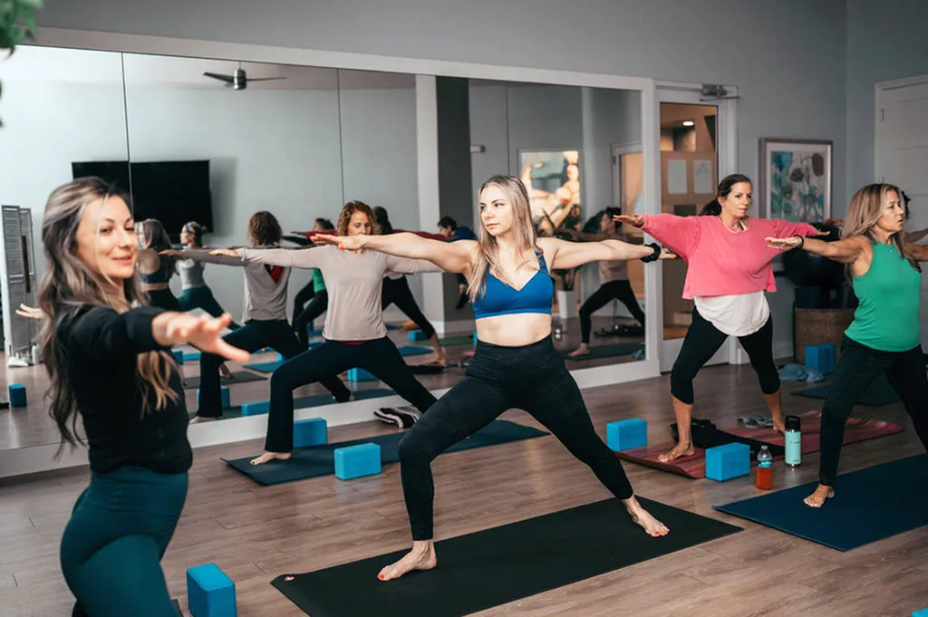 Inviting yoga studio with a mirrored wall where lively participants practice warrior poses on mats, creating an energetic and harmonious atmosphere.