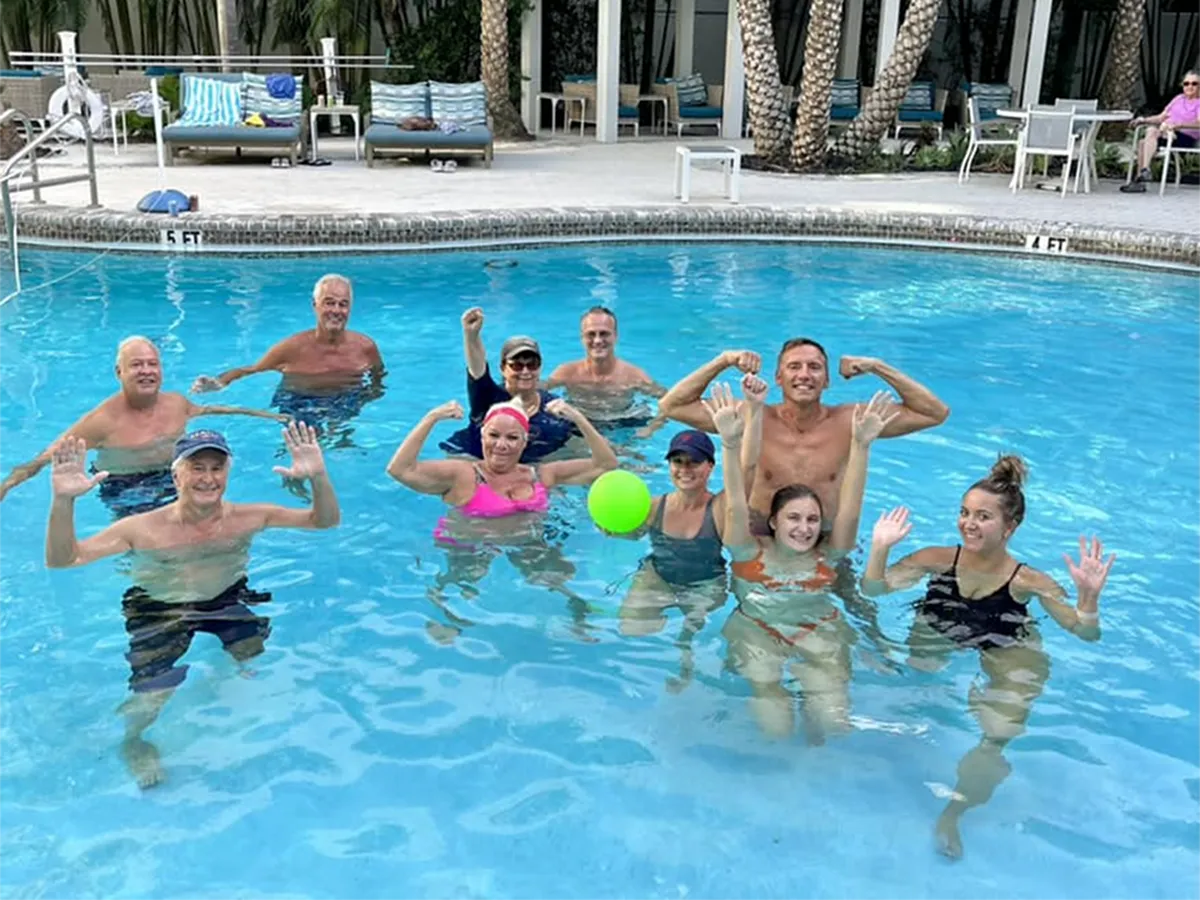 Vibrant pool scene showcasing a group of joyful people enjoying a sunny day, lush palm trees and relaxing loungers in the background.