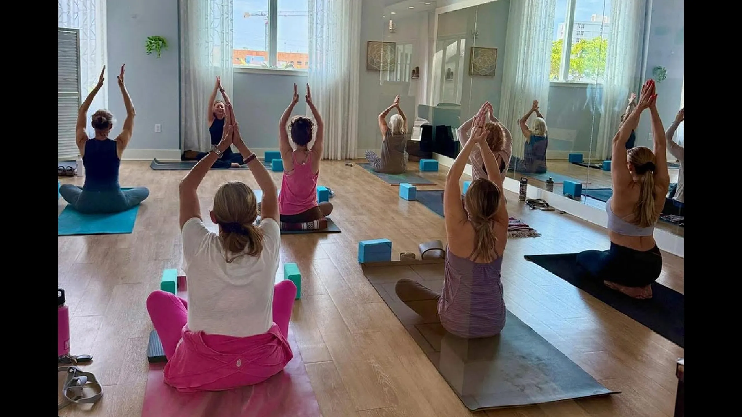 Serene yoga class in a bright, modern studio with wooden floors and large windows, offering a calming and rejuvenating experience.