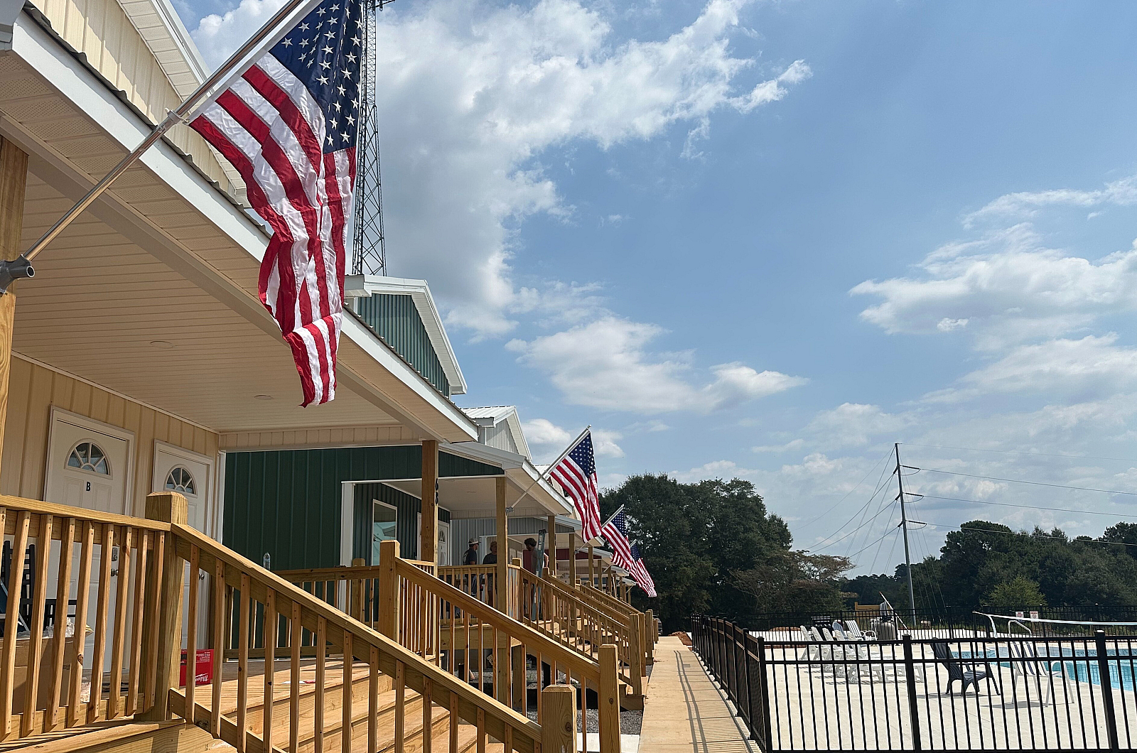 Charming residential complex with patriotic flair, showcasing a row of modern homes with inviting wooden porches adorned with American flags beside a serene community pool.