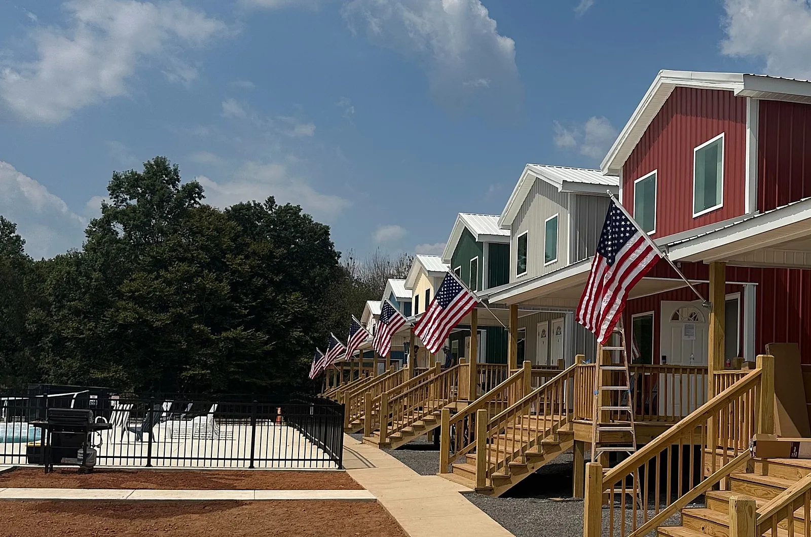 Charming row of colorful modern homes with inviting porches and American flags, set against a bright blue sky.