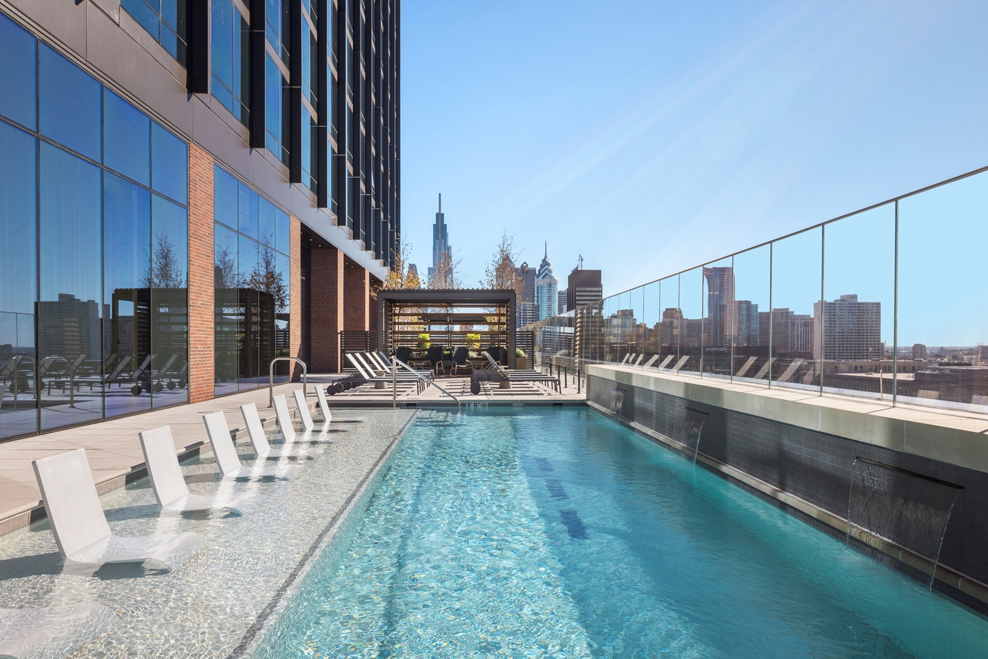 Luxurious rooftop pool with stunning city skyline views, featuring modern lounge chairs and sleek glass railings.