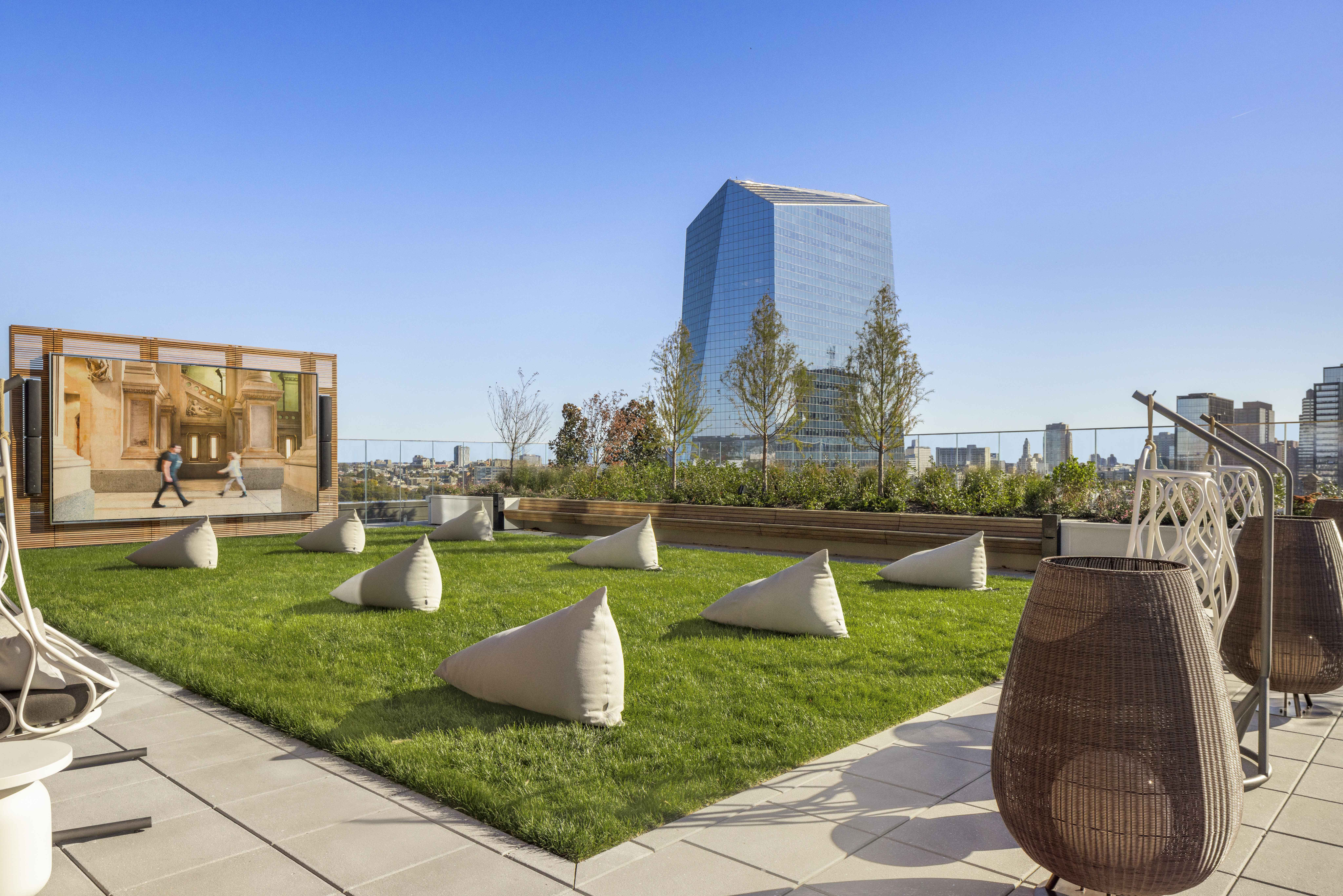 Luxurious rooftop terrace with modern lounge chairs, lush lawn, and panoramic city views, featuring a large outdoor screen for entertainment.